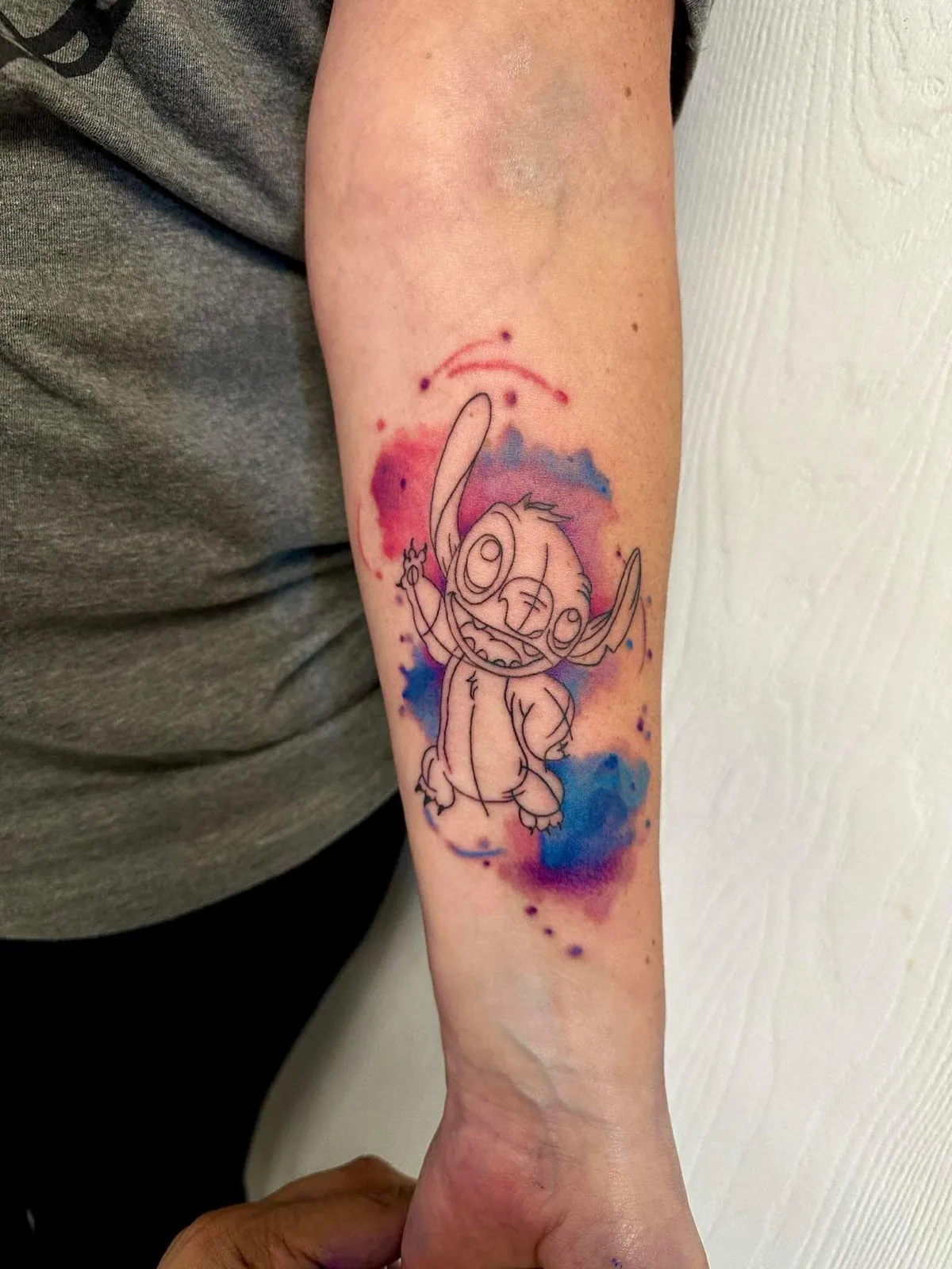 Custom watercolor Stitch tattoo on forearm with pink and blue splash